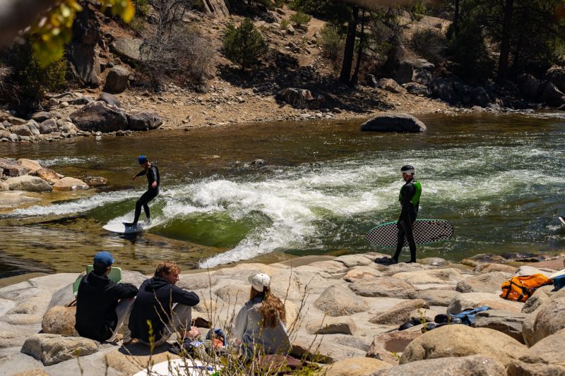 Surfer riding river wave near rocky shore