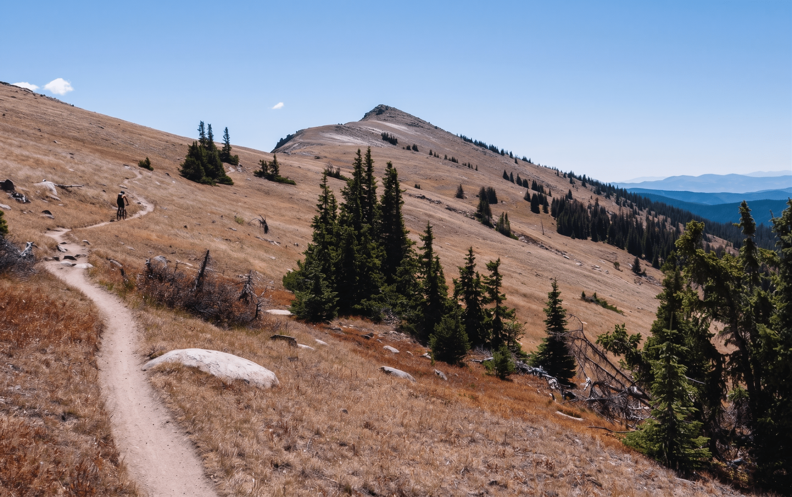 Cyclist riding mountain trail through grassy hills