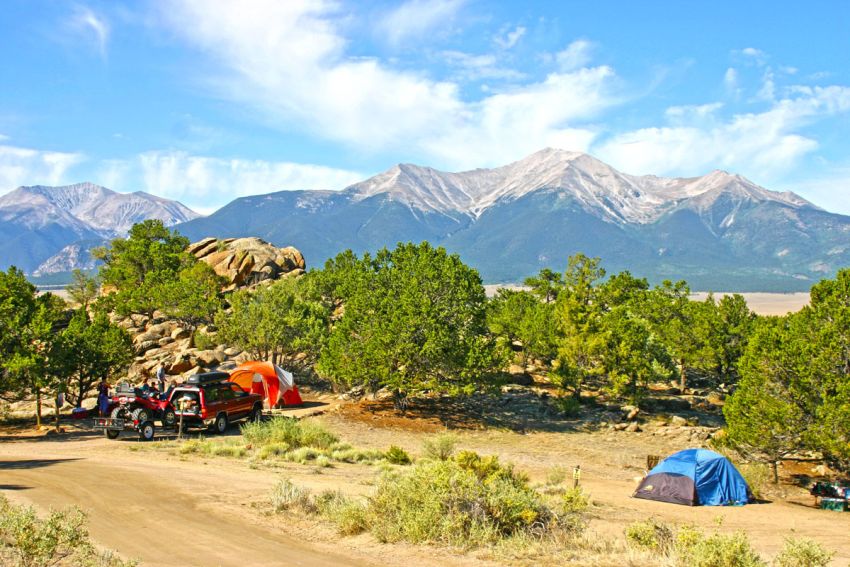 Camping in Colorado, against mountains and a blue sky, next to a dirt road