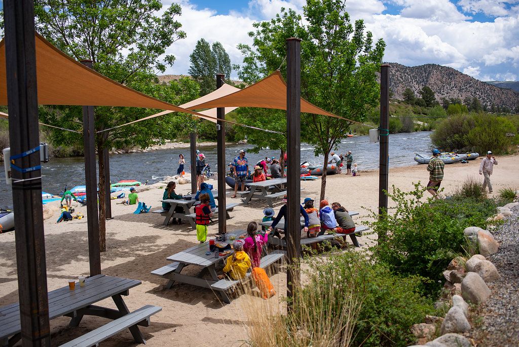 People enjoying a riverside picnic with kayaks nearby.