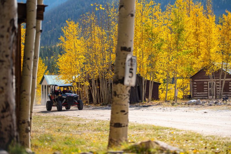 Golden aspen trees beside rustic cabins and an off-road vehicle