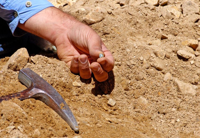 Rockhound showing off a find in his hand, against a pile of dirt and stone