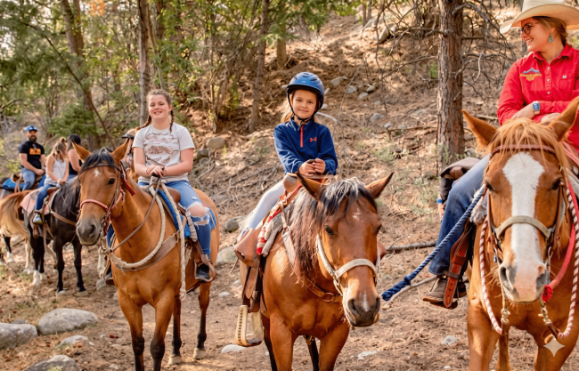 Children horseback riding on wooded trail