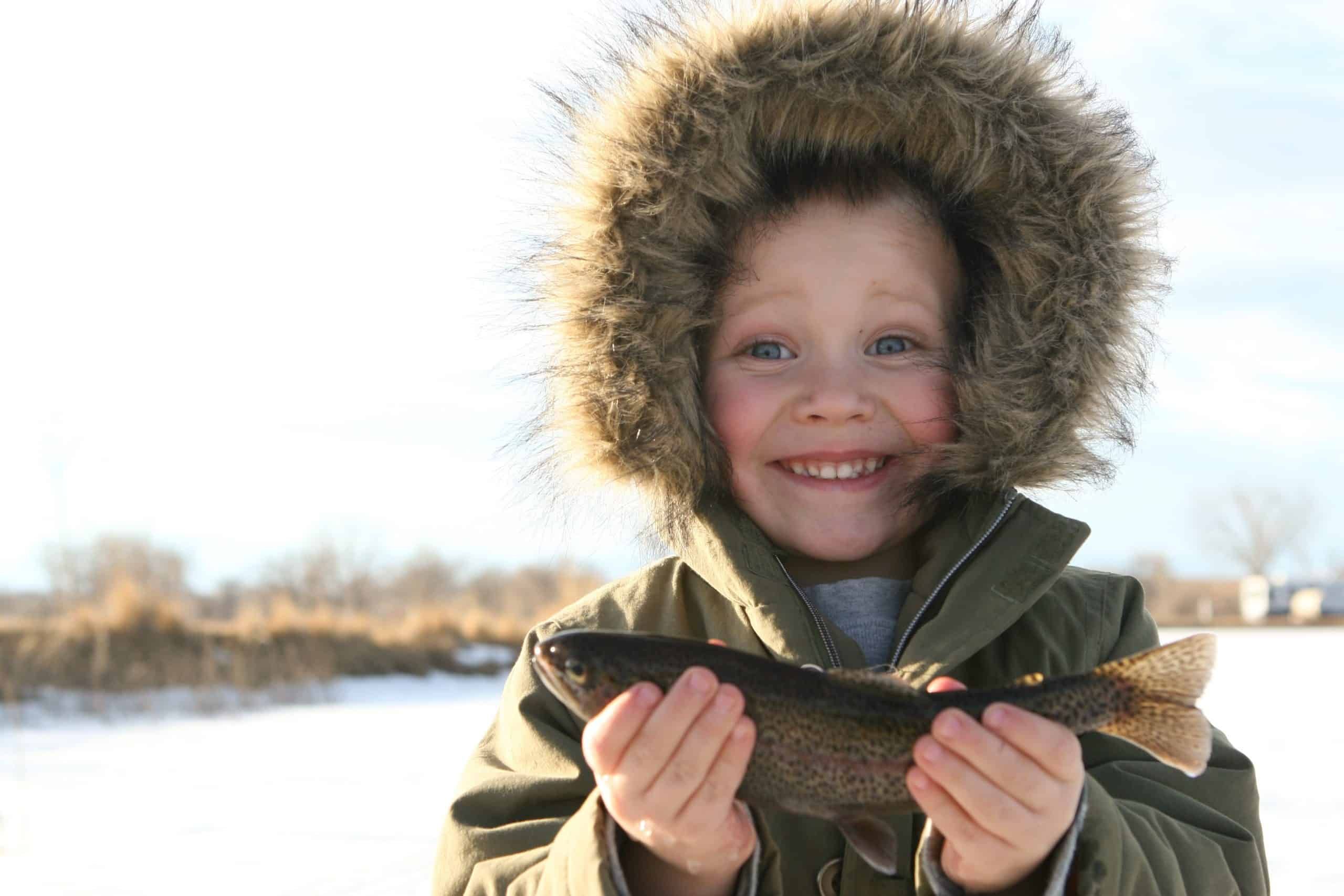 Smiling child holding fish in snowy landscape