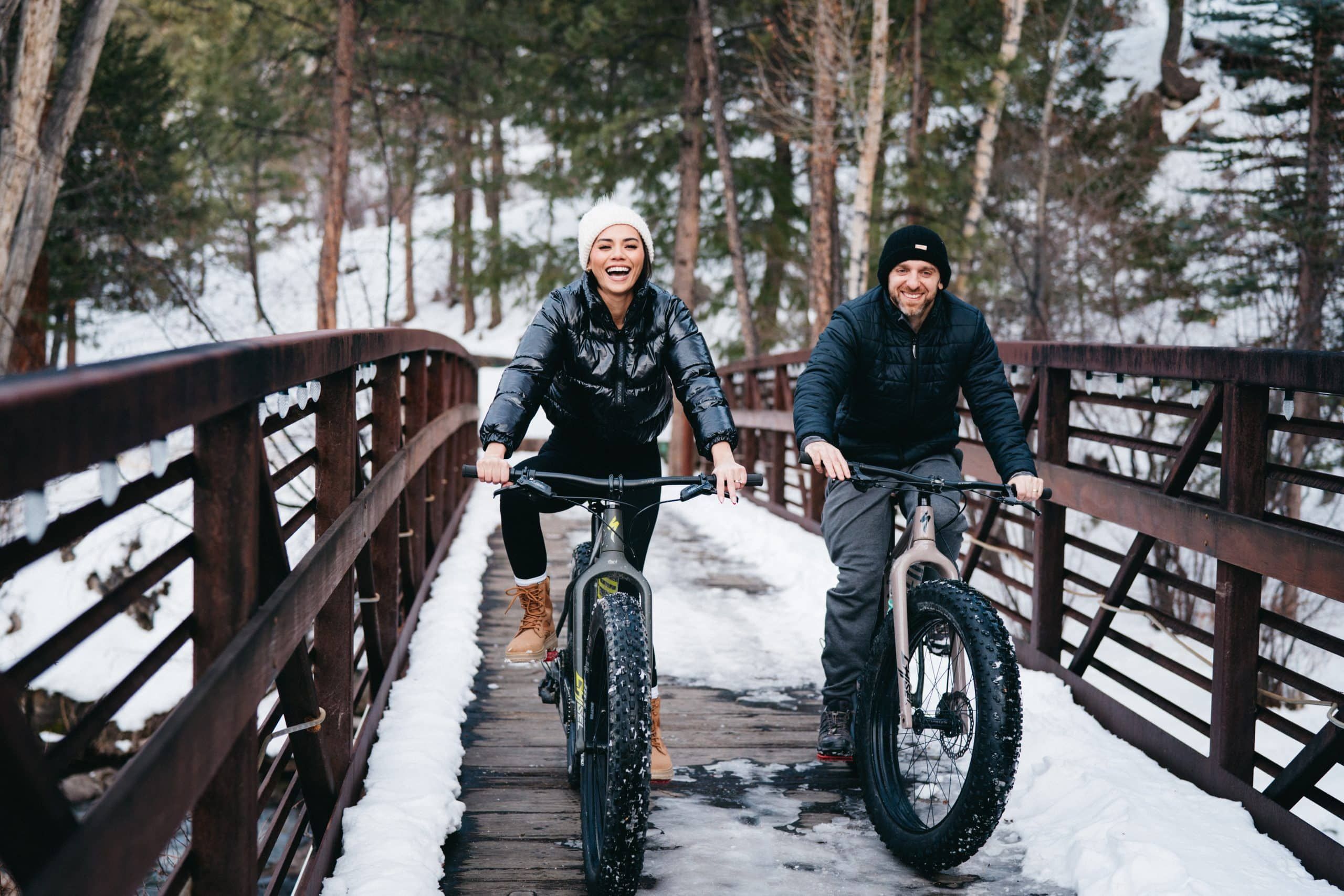 Couple riding fat-tire bikes on snowy bridge