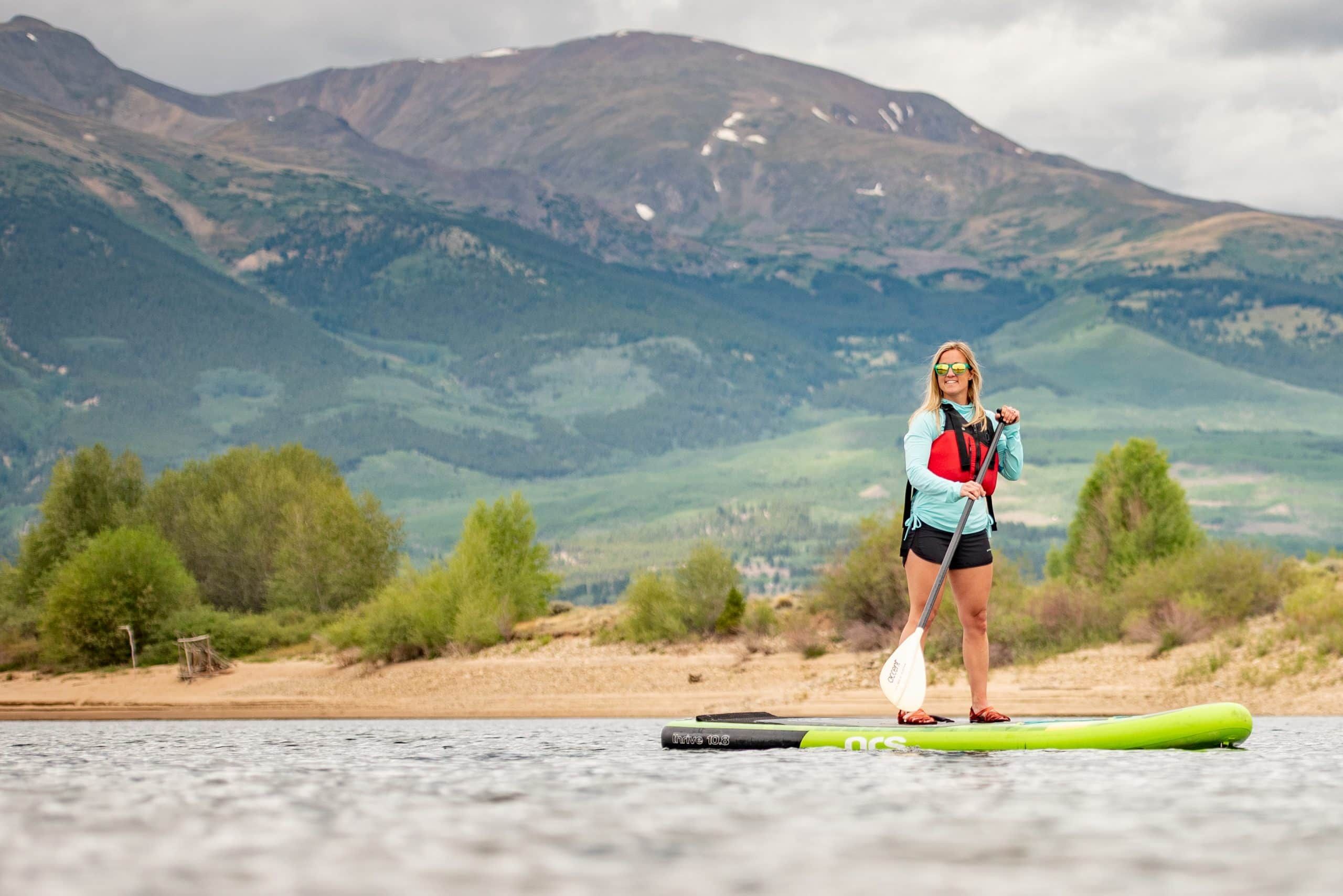Woman paddleboarding on mountain lake with scenic backdrop