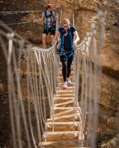 Two hikers crossing narrow suspension bridge on cliff