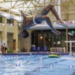 Boy mid-backflip above indoor swimming pool