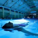 Person floating in illuminated indoor swimming pool