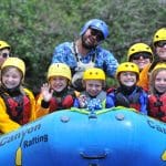 Family whitewater rafting group smiling in helmets
