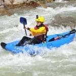 Kayaker navigating whitewater rapids in blue inflatable kayak